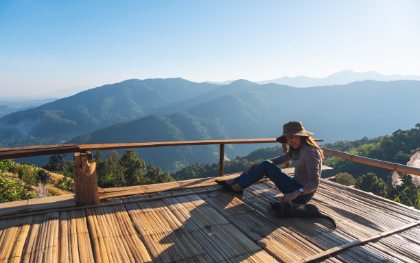 一个女游客坐在和猫玩耍的木制阳台上，蓝天和美丽的山景图片下载