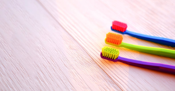 三把彩色的牙刷放在一个木制的背景和早晨的阳光。家庭牙科概念。有选择性的重点。本空间图片下载