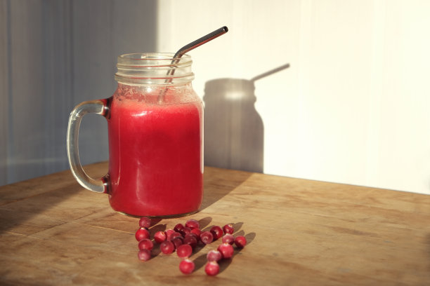 蔓越莓汁在梅森瓶和新鲜的浆果在木桌和阴影在白色墙壁上。自制的维生素饮料。图片下载