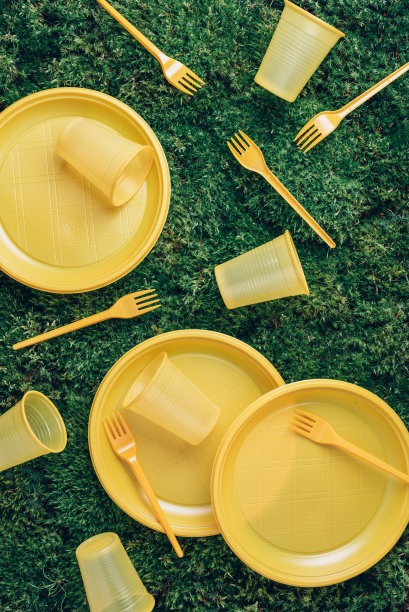 一次性塑料餐具——塑料盘子，叉子，勺子，刀。黄色的塑料餐具在绿草、青苔的背景上。前视图。副本的空间。环境污染。禁止使用一次性塑料。横幅图片下载