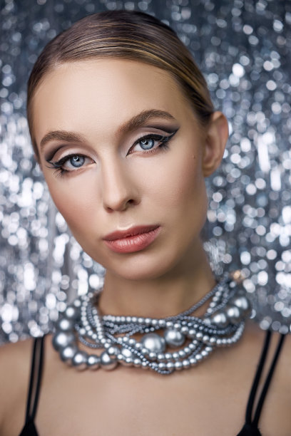一个金发女人的眼睛化妆在一个闪亮的背景。一个女人的肖像与项链围绕她的脖子特写，完美的眼妆，脸护理图片下载