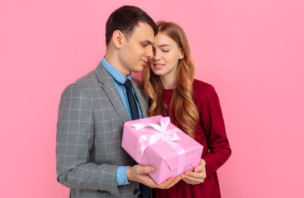 情人节庆祝，快乐的年轻夫妇，男人和女人在粉红色的背景礼物盒图片下载