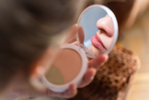 年轻女子化好妆，对着镜子看着自己的嘴唇图片下载