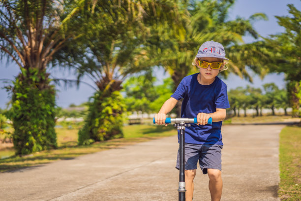 孩子在公园踢踏板车。孩子们学滑旱冰。小男孩在阳光明媚的夏日滑冰。儿童在安全住宅区街道的户外活动。学龄前儿童的积极运动图片下载
