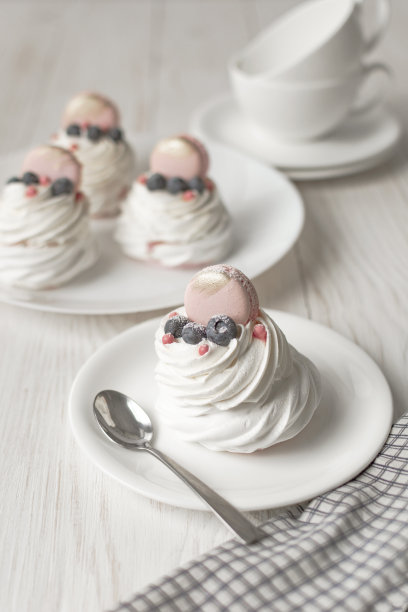 白色背景上有新鲜浆果的Pavlova蛋白酥饼。木桌上放着茶杯和餐巾图片下载