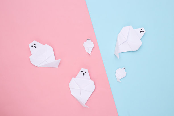 粉蓝背景上的折纸鬼。手工制作的万圣节装饰品。俯视图图片下载