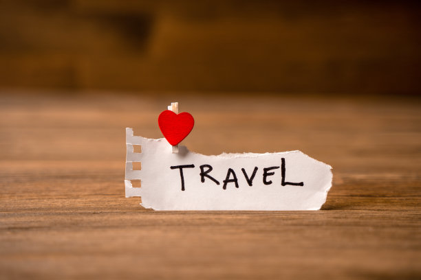 一张粗糙的纸，上面写着“旅行”，木制背景上有一颗红心。旅游的概念图片下载