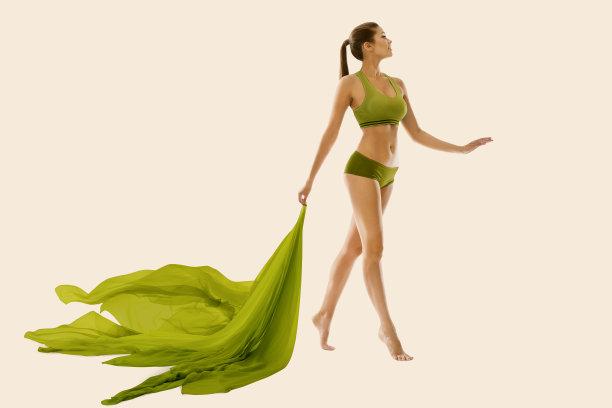 美丽女人苗条的身体，腿身体保健，皮肤治疗。绿色织物飞行。米色背景图片下载