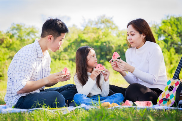 幸福的家庭野餐。亚洲父母(父亲，母亲)和小女孩吃西瓜，有乐趣和享受自己一起在野餐布在花园在一个阳光明媚的日子素材图片