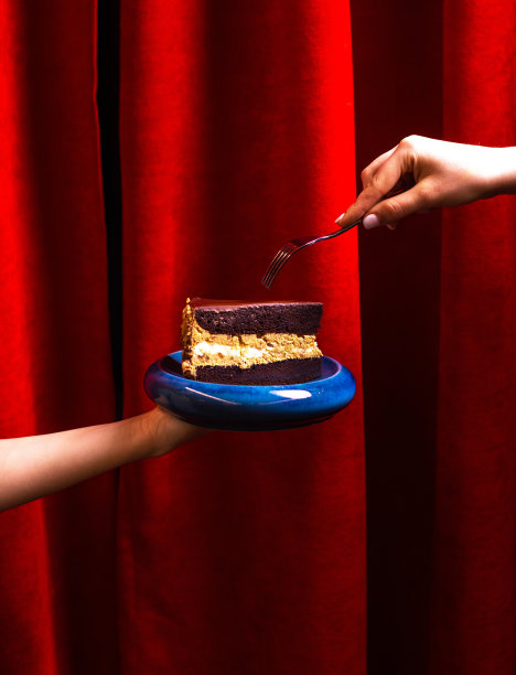 在红色的窗帘背景上，女性手拿着一个托盘，上面放着一块美味的巧克力蛋糕图片下载