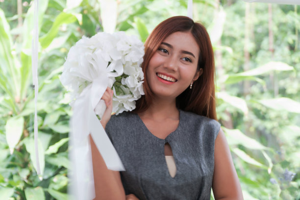 美丽的亚洲年轻女子站在手持一束白花微笑幸福。图片下载