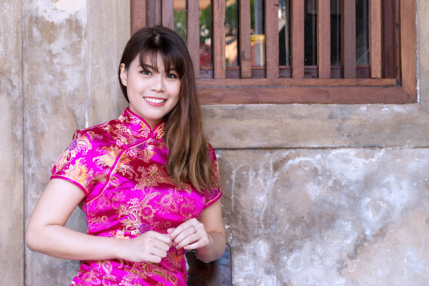 在中国新年庆祝活动中，穿着深粉色旗袍的迷人年轻女子看着照相机。庆祝活动的概念。图片下载