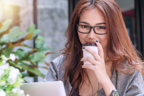 成功的商业工作目标概念。微笑的商务女性戴着眼镜工作，手提电脑，手里拿着一杯咖啡，看着相机在咖啡店cafÃ©。图片下载