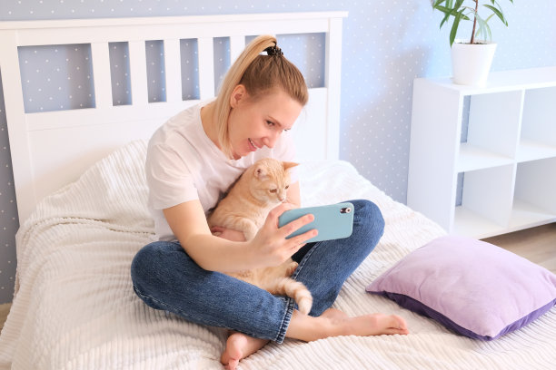 漂亮女人坐在床上摆姿势，手里拿着智能手机图片下载