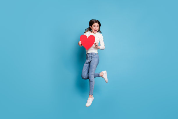 长照片漂亮的波浪形女士穿白色毛衣跳着红纸心孤立的蓝色背景图片下载