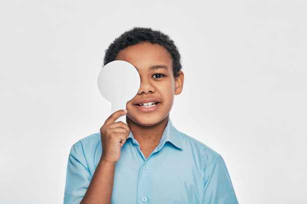 非裔美国男性儿童，用眼科工具遮住一只眼睛，在白色背景上做眼部检查图片下载