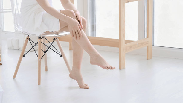 女人抚摸她光滑柔软的双腿，享受美容程序。年轻的亚洲妇女涂抹霜和乳液，触摸脚在床上干。本空间图片下载