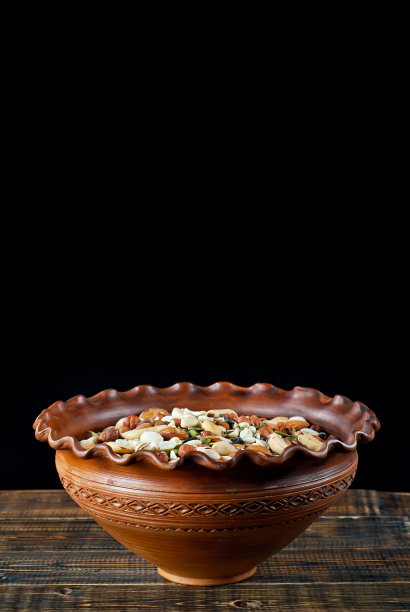 很多种类的坚果都可以近距离观察。木板上不同坚果的纹理。一个粘土碗放在棕色的桌子上。图片下载