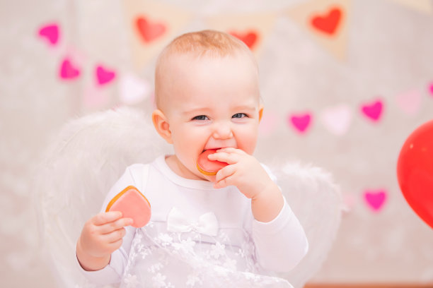 一个快乐的小女孩带着白色的羽毛翅膀正在吃心形的饼干，这是情人节的象征图片下载