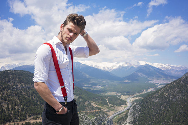 一个背着吊带的年轻人在山顶摆姿势。图片下载