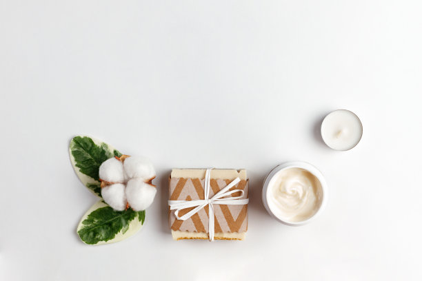 化妆品和自我保健。白色的背景上放着一朵绿叶棉花、手工制作的肥皂、一罐奶油和一支蜡烛。平铺和复制空间图片下载