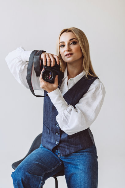 一位美丽的女摄影师，穿着牛仔休闲套装和宽松袖子的白色衬衫，手里拿着相机。爱好。软选择聚焦。图片下载