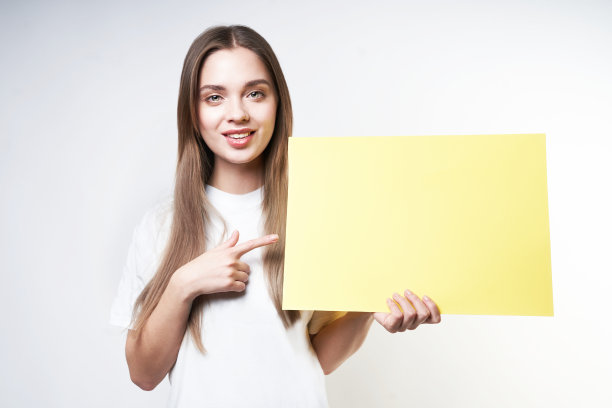 一位身穿白色t恤、灰色背景上举着黄色标牌的金发美女图片下载