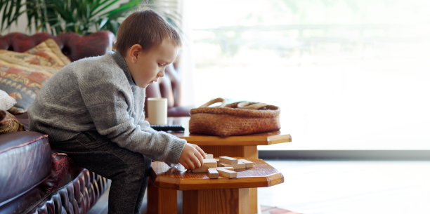 幼儿园里可爱的小男孩在家里玩着积木桌游戏。男孩用木块搭一座塔，留在家里横幅图片下载