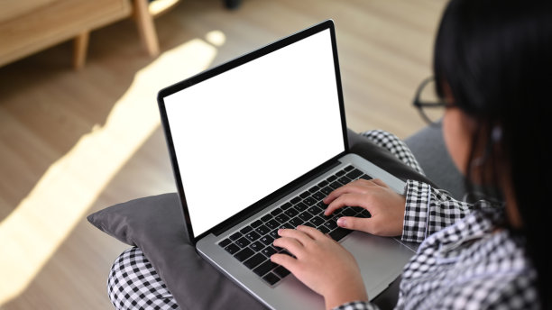 一个年轻的亚洲女孩坐在家里的沙发上使用笔记本电脑的镜头。图片下载