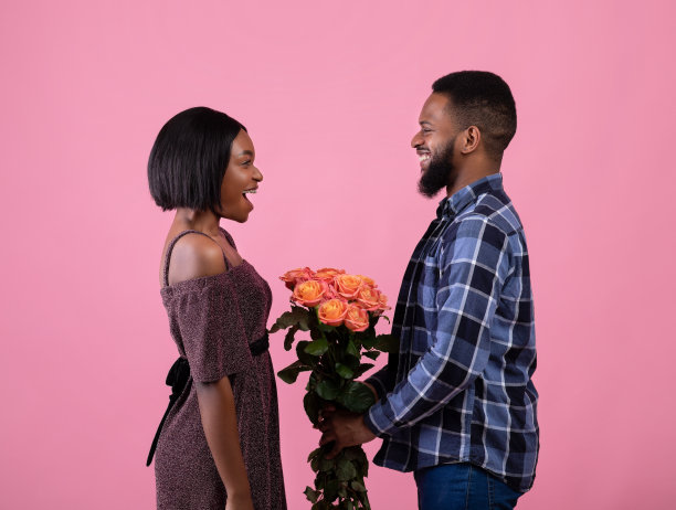 侧面的正面黑人男子在粉红色的工作室背景上向他的女朋友献花。情人节图片下载
