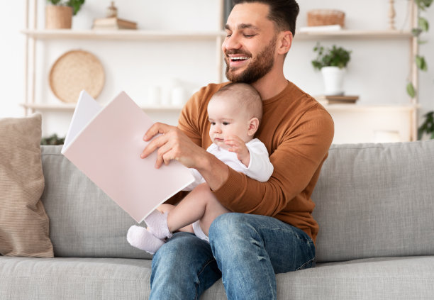 年轻的父亲在家里读给小婴儿看的书图片下载