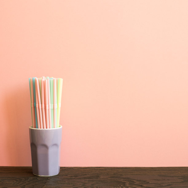 木桌上的杯子里装着五颜六色的吸管。粉红色的背景图片下载
