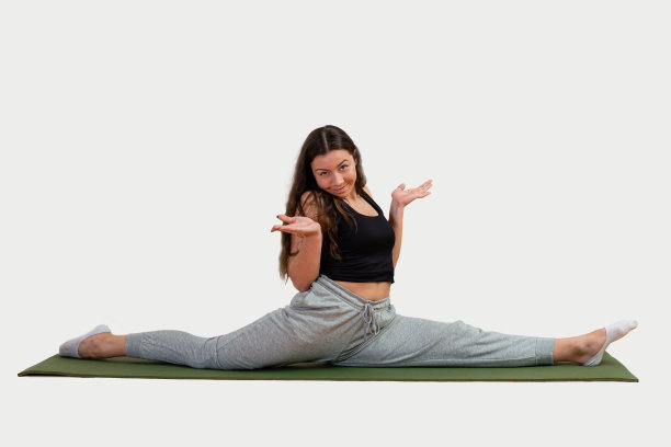迷人的年轻女子坐在绿色垫子上表演劈叉，孤立在白色上图片下载