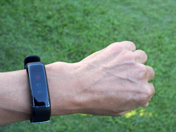 近距离追踪亚洲男性手腕上的智能手环，以绿草地为背景图片下载
