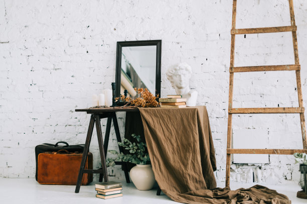 白色的客厅内饰有木桌，棕色的织物和大镜子，靠近墙壁的木梯。的作文图片下载