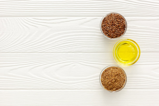 用勺子和碗盛亚麻籽，配上一瓶亚麻籽油和亚麻籽面粉图片下载