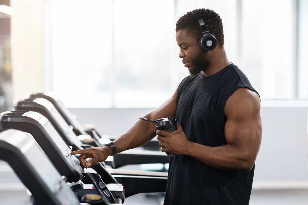 肌肉发达的黑人喝着蛋白质饮料站在跑步机上图片下载