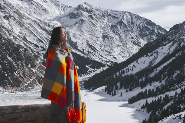 年轻的女孩披着五颜六色的毯子，在冬日雪山的背景下。风景优美的风景。自然，旅行，冒险，徒步旅行。图片下载
