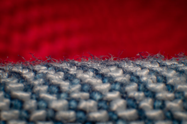 牛仔布合成纤维照片纤维之间有空隙。编织整齐，蓝白纤维，高倍放大，超微距。背景是模糊的红布。图片下载