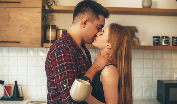 褐发男人在厨房边喝茶边亲吻他的姜黄色的有雀斑的妻子图片下载