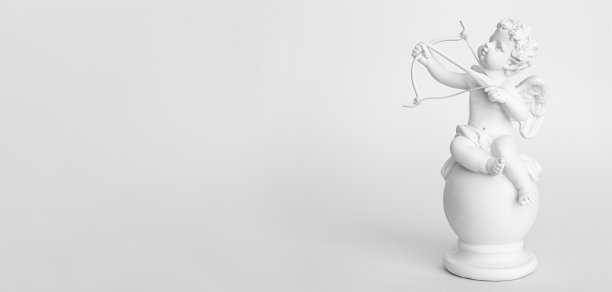 横幅。粉红色背景上带着蝴蝶结的天使丘比特小雕像。情人节图片下载