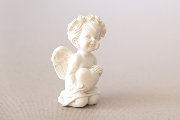 粉红色背景上带着蝴蝶结的天使丘比特小雕像。情人节图片下载