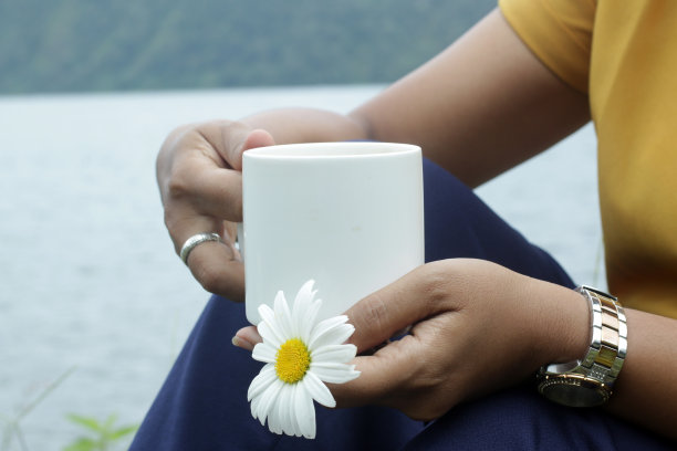 一个女人独自坐在户外，手里拿着白色的咖啡杯和一朵花。图片下载