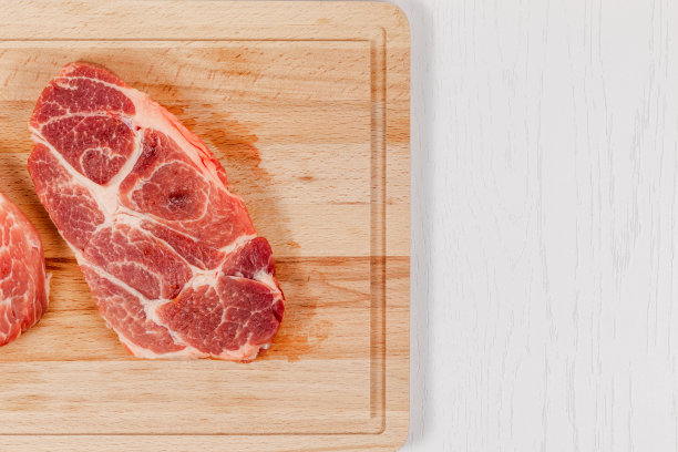 新鲜的生猪肉排放在坚实的山毛榉木砧板上，放在白色的桌子上图片下载