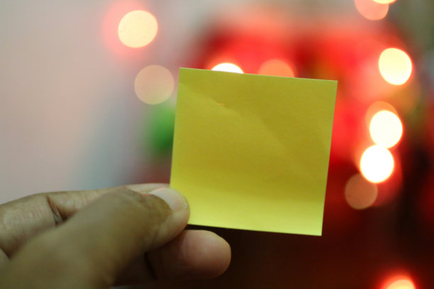 手里拿着空白的黄色纸和彩色的散景背景。图片下载