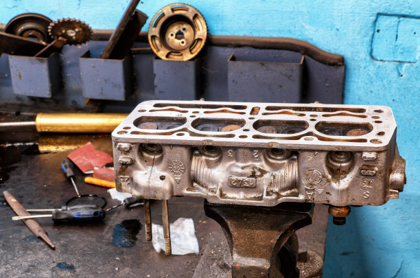 机修工正在工作台上修理一个旧的汽缸盖。在模糊的背景其他工具，如砂纸，螺丝刀和锉刀。这是艺术、手工艺和工作的完美照片。图片下载