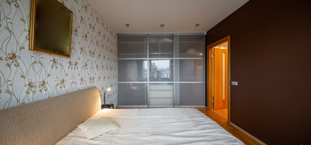 现代公寓卧室的现代室内。舒适床的侧视图。灯在床头柜上。滑动玻璃门衣柜。图片下载