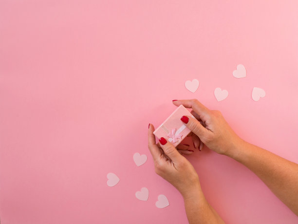 女人手握礼物，粉色背景上的心。图片下载