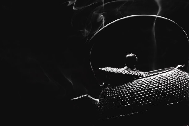 古董茶壶与热气腾腾的茶在黑色的背景。图片下载
