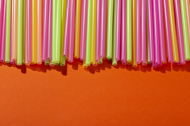 橙色背景上的彩色小管用于果汁和鸡尾酒。空间的文本。图片下载